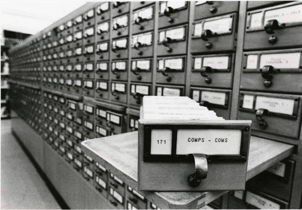 A close-up on a card catalog drawer for "COMPS-COMS" in front of the rest of the card catalog.