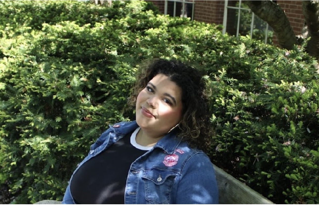 Kaylin Reynolds sitting on a bench in front of a leafy bush on a bright sunny day.
