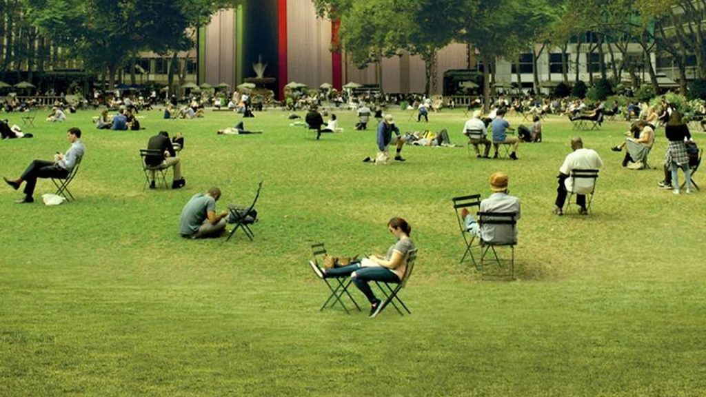 A bunch of people sitting by themselves in a big grassy field with reading materials and folding chairs.